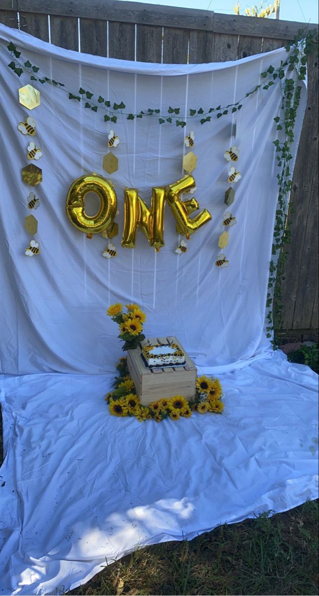 a table with a cake and balloons on it in front of a white backdrop that says one