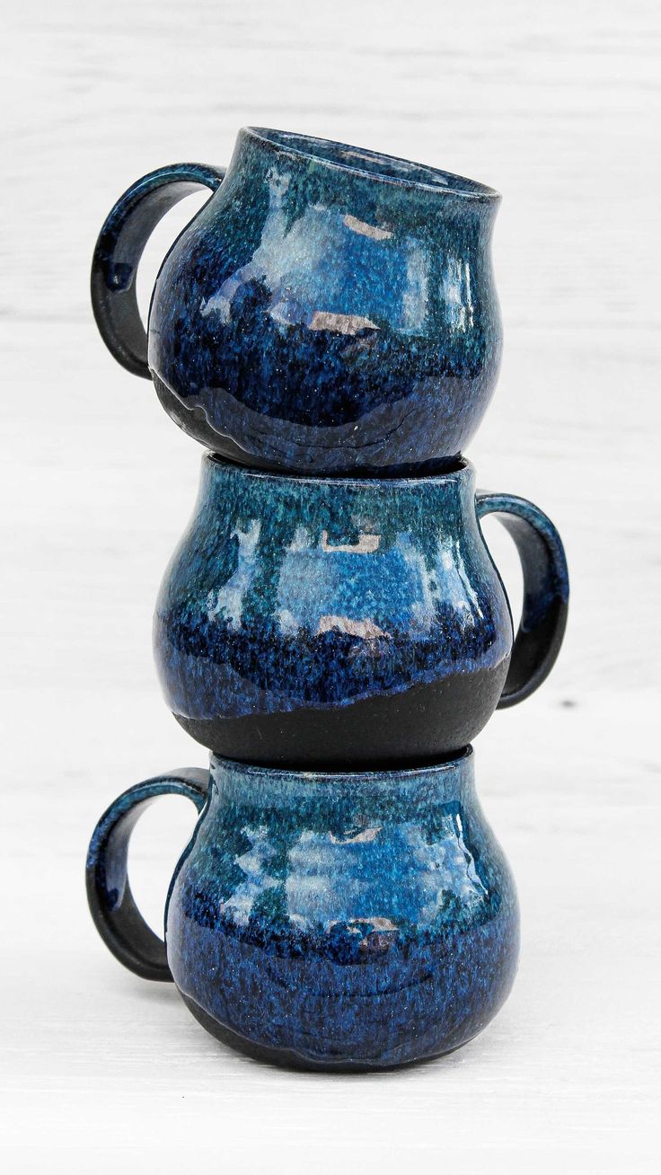 three blue mugs stacked on top of each other in front of a white background