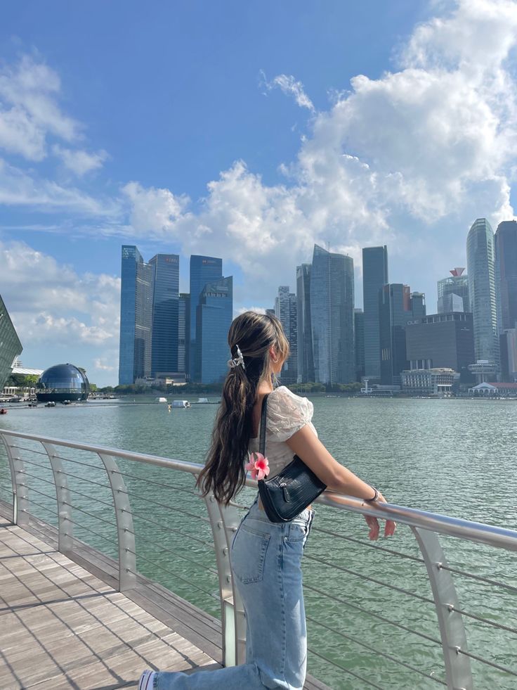 a woman standing on the edge of a pier looking at the water and buildings in the background