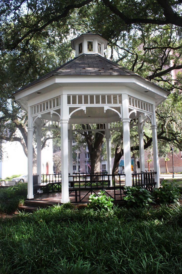 a white gazebo sitting in the middle of a lush green park