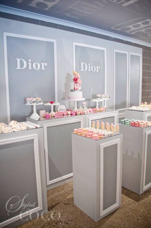 the dessert table is set up in front of the dior sign and display cases