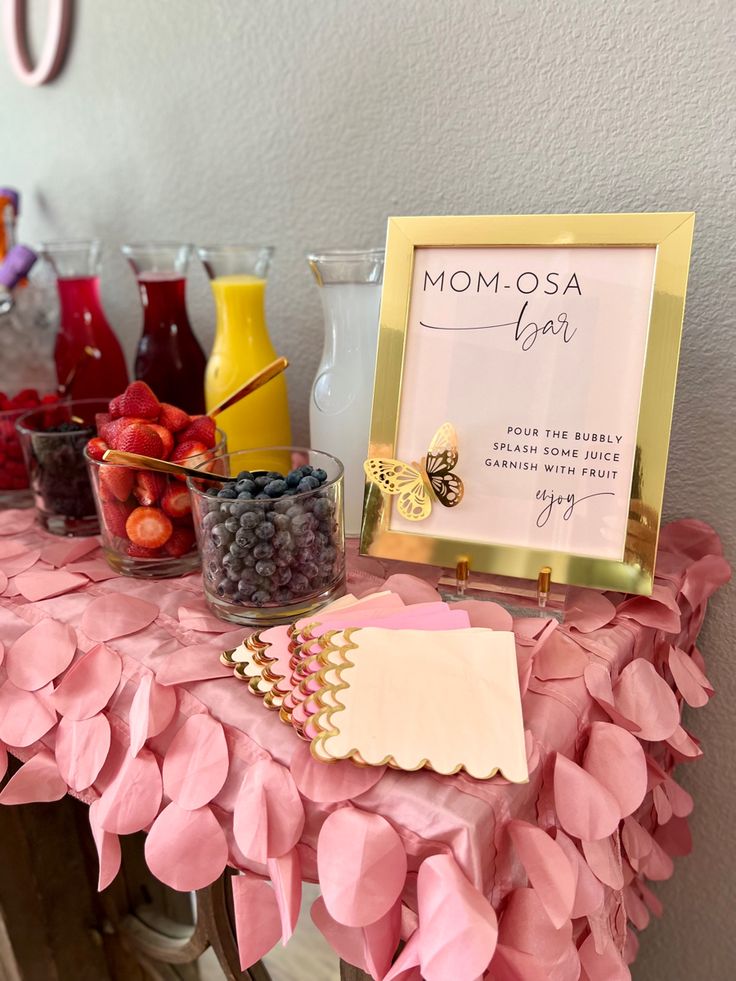 a pink table topped with lots of fruit and drinks next to a sign that says mom osa