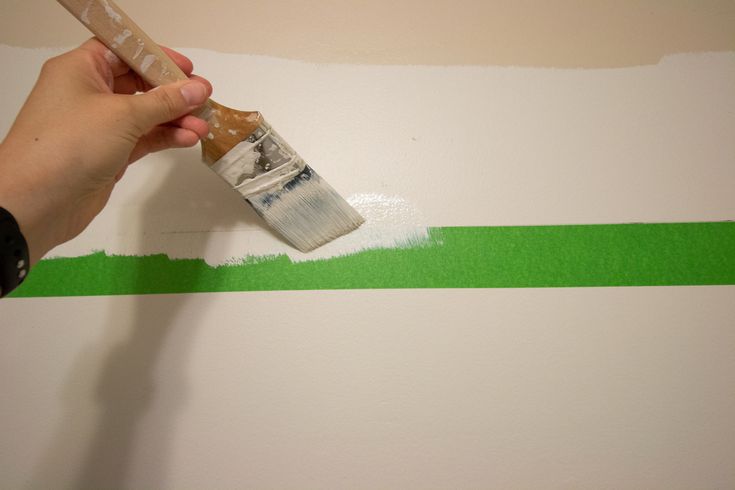 someone is painting the wall with green tape and a paintbrush in their left hand