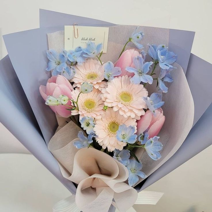 a bouquet of blue and pink flowers with a note attached to the back of it