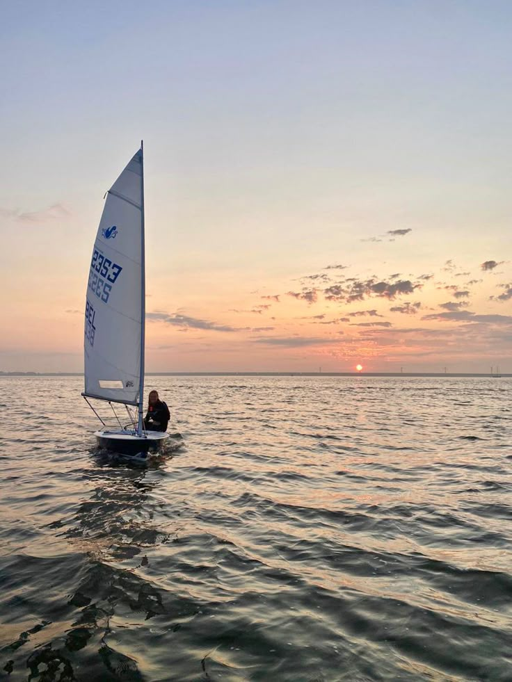 a person on a sailboat in the ocean at sunset