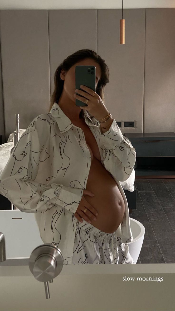 a pregnant woman takes a selfie in the bathroom mirror while holding her cell phone