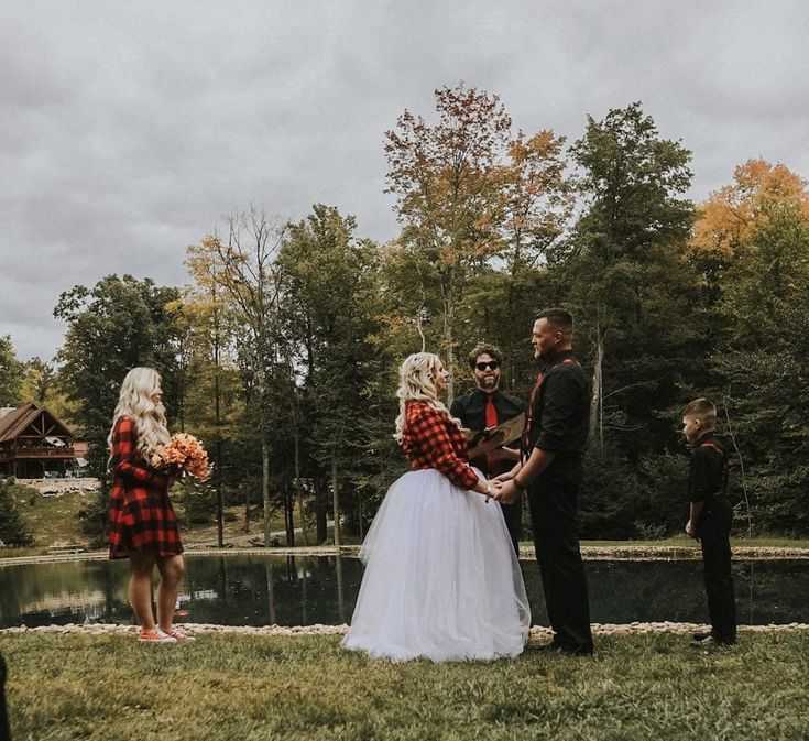 a bride and groom standing in front of a lake with their wedding party looking on