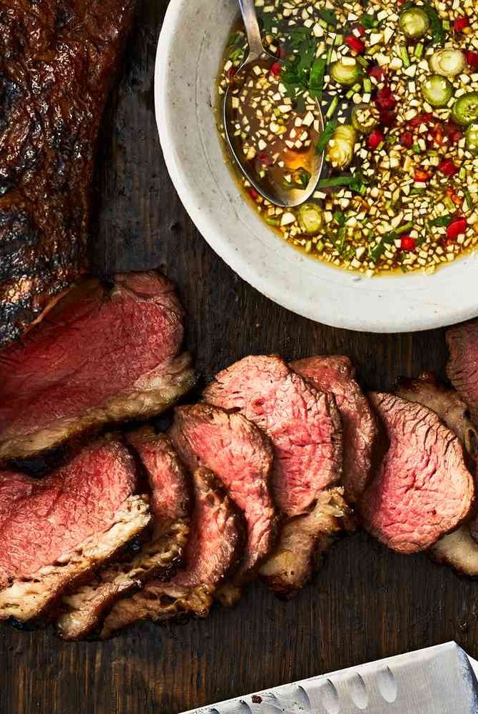 sliced steak and vegetables on a cutting board next to a knife, bowl of soup