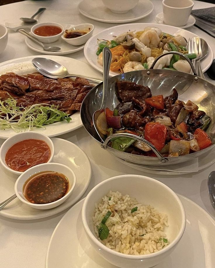 a table with many plates and bowls of food on it, including rice, meats, vegetables, and sauces