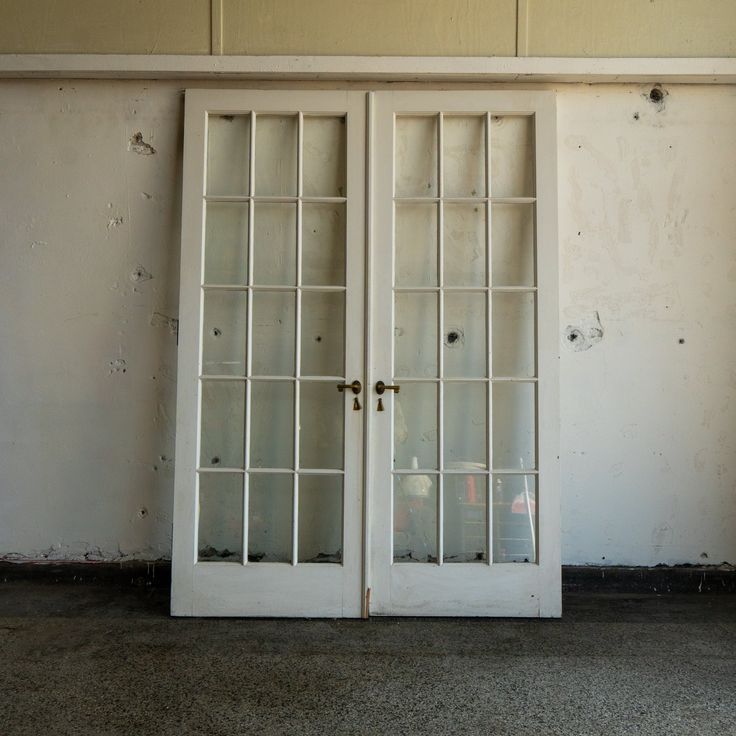 two white double doors with glass panes in an empty room next to a wall