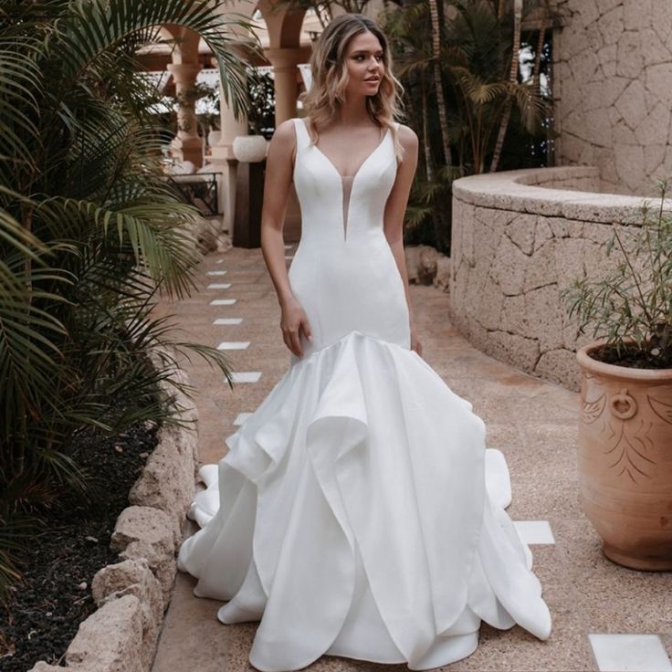 a woman in a white wedding dress is standing on the steps next to a potted plant