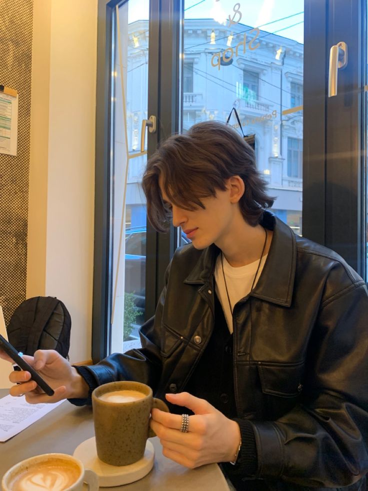 a man sitting at a table with a cup of coffee looking at his cell phone