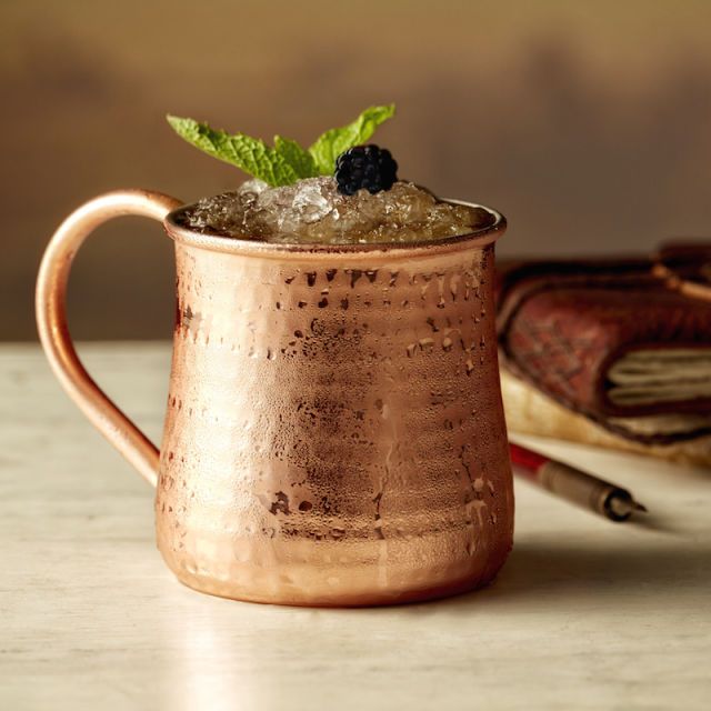 a copper mug filled with ice and mint sitting on top of a table next to an open book