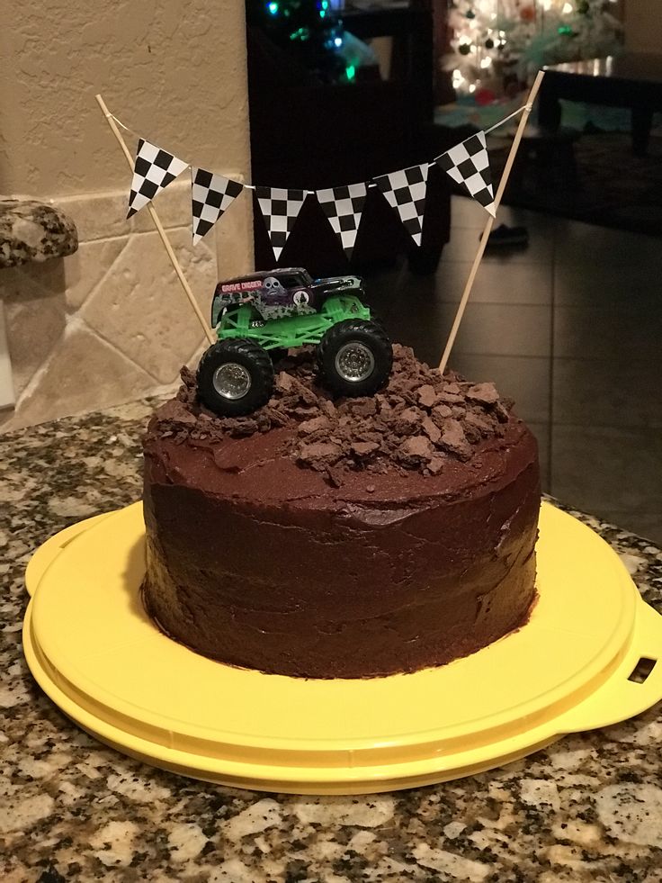 a chocolate cake with a green truck on top and checkered flags in the background