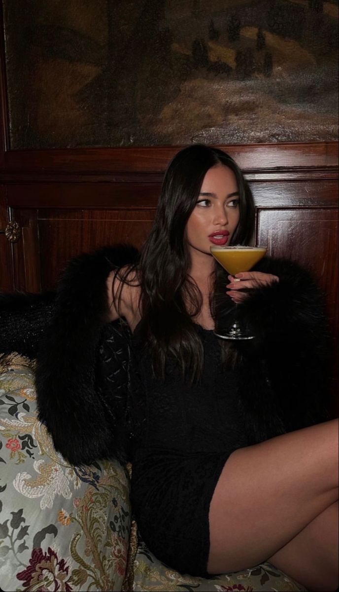 a woman sitting on top of a bed holding a glass of orange juice in her hand