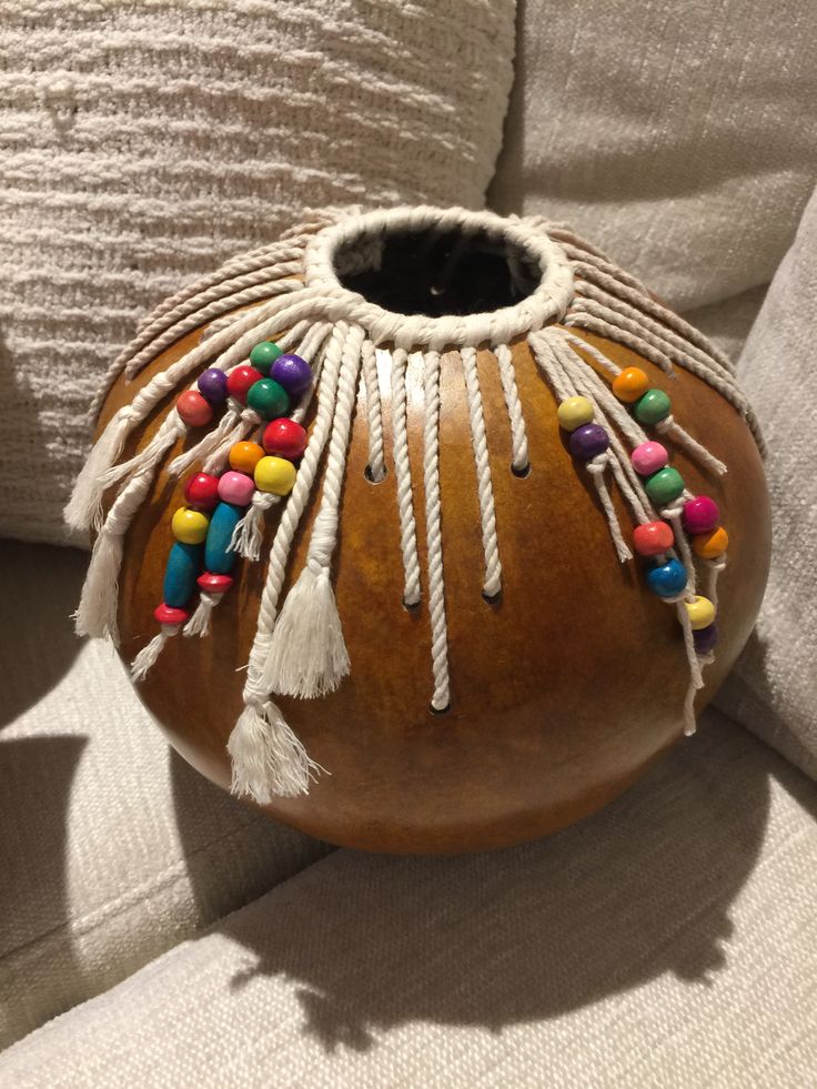 a wooden vase with colorful beads and tassels on the bottom sitting on a couch