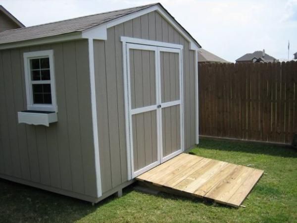 a small shed sitting in the grass next to a wooden deck and fenced yard