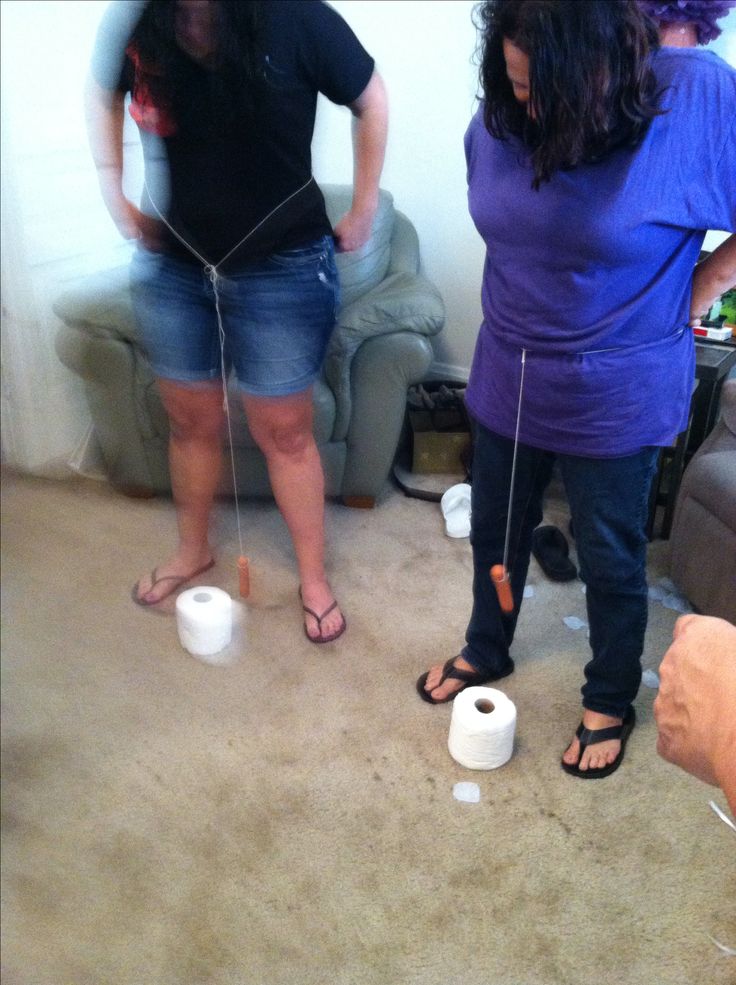 two women standing next to each other in a living room with toilet paper on the floor