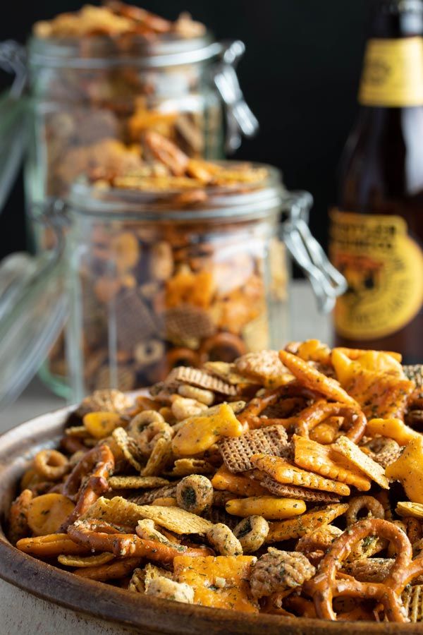 a bowl full of cheesy snack mix next to two bottles of beer on the table