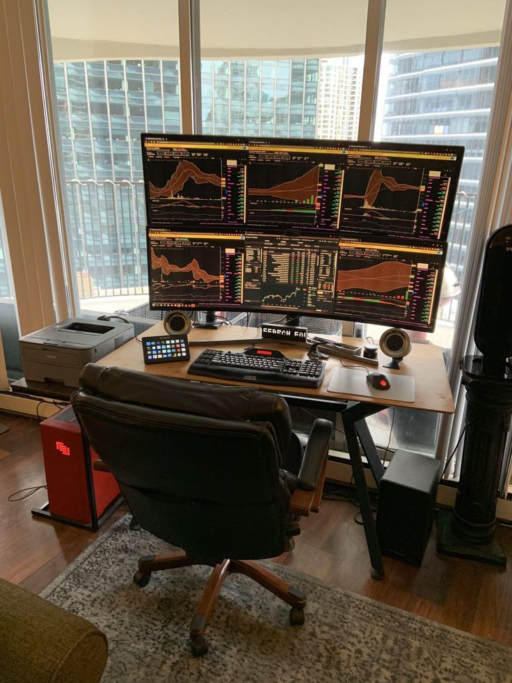 a desk with two monitors and a keyboard on it in front of a large window