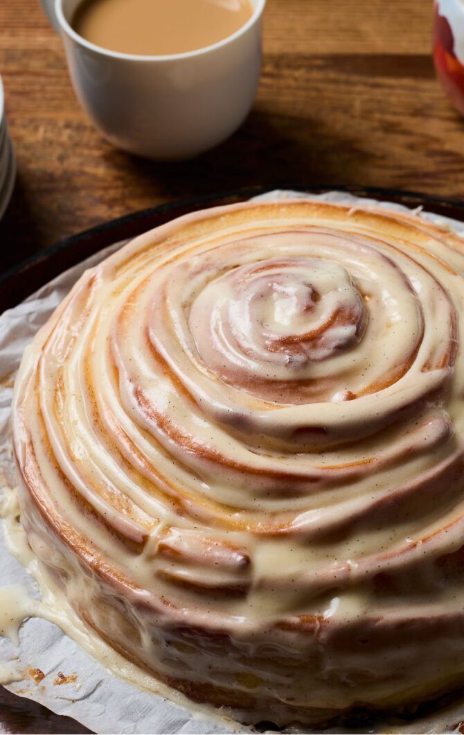 a cake sitting on top of a pan covered in icing next to a cup of coffee