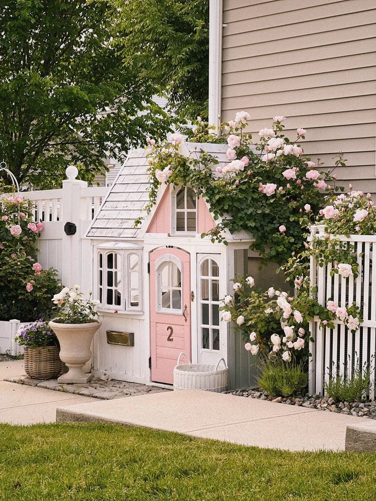 a pink and white doll house in the yard with flowers on it's roof