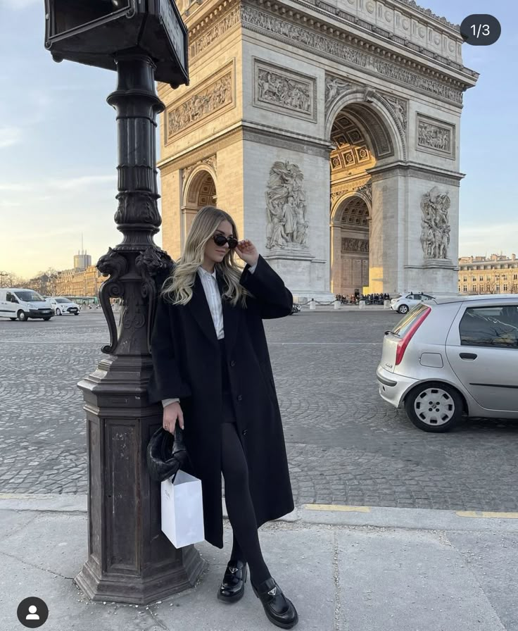 a woman standing next to a lamp post in front of the arc de trioe