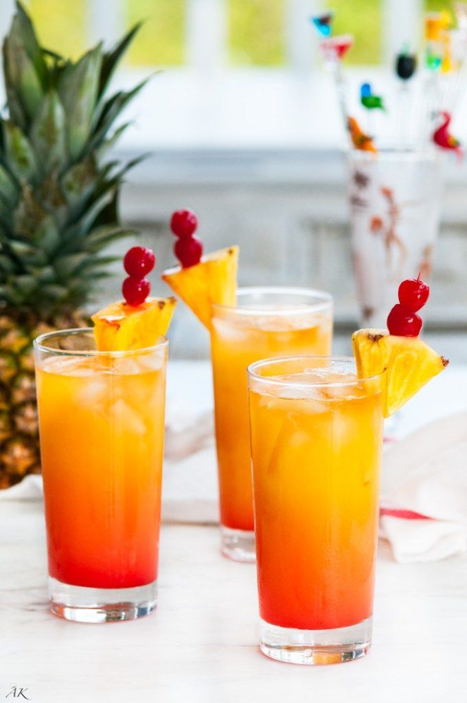 three glasses filled with drinks sitting on top of a table next to a pineapple