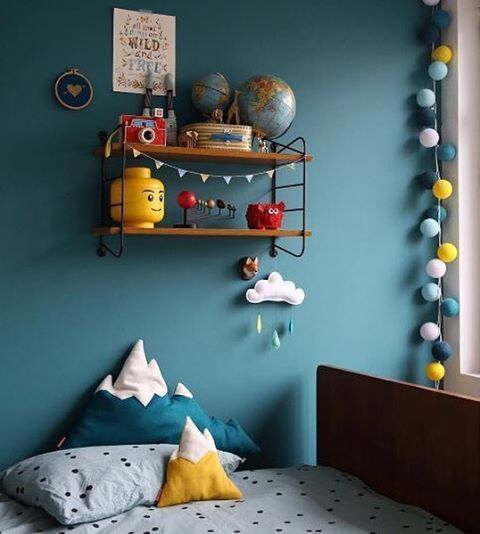 a bed room with a neatly made bed next to a blue wall and shelves filled with toys