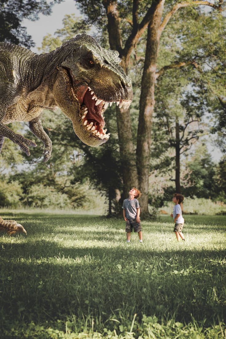 two children are playing in the grass with an adult dinosaur