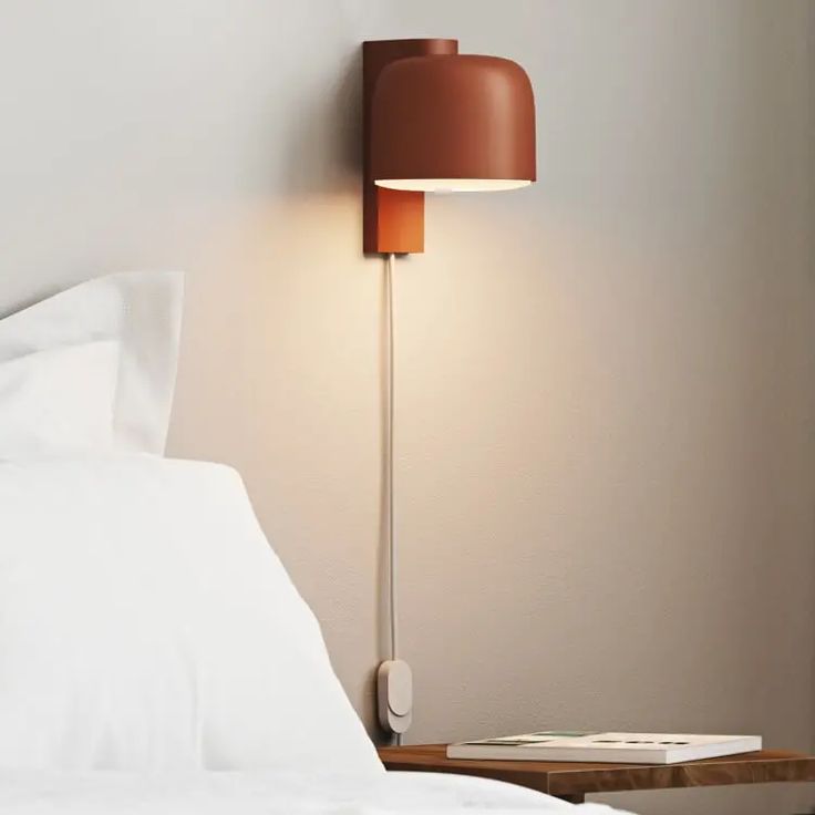 a lamp that is on the side of a bed next to a night stand with a book