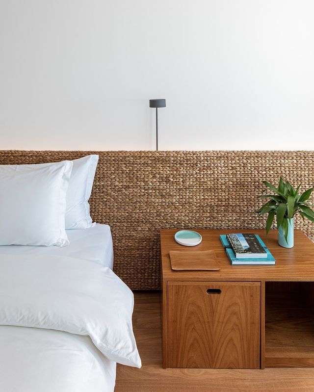 a bed with white sheets and pillows next to a night stand on wooden flooring