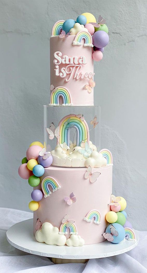 a three tiered cake with rainbows and clouds on the top is decorated in pastel colors