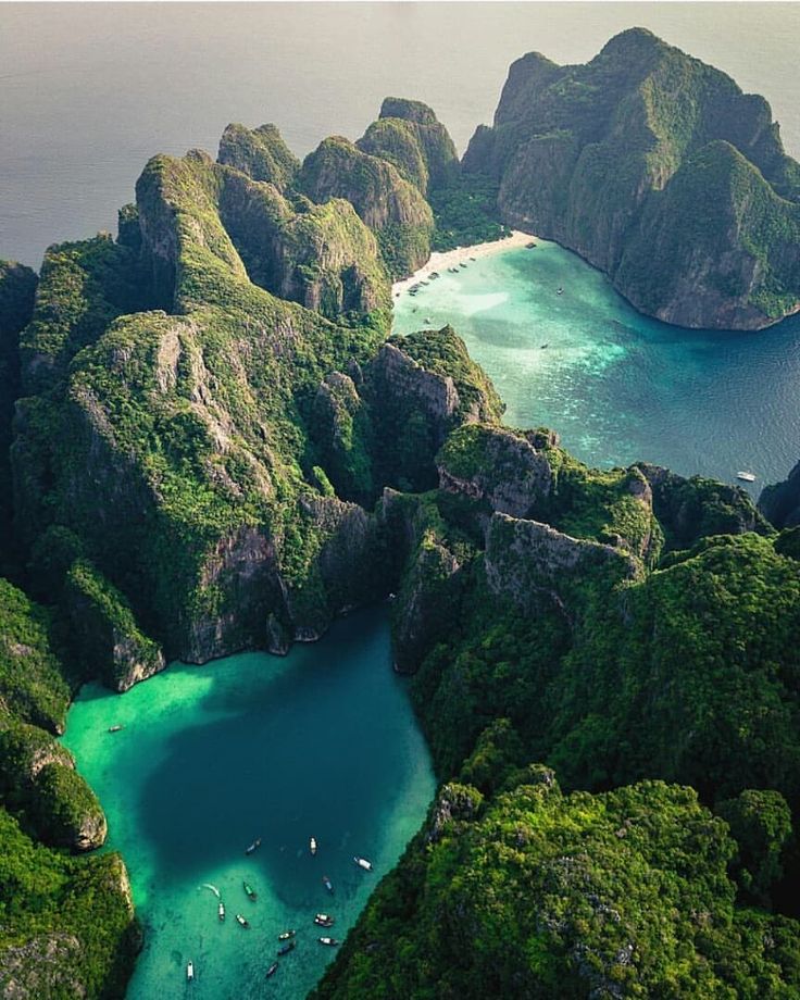 an aerial view of some green mountains and water with boats in the water near by