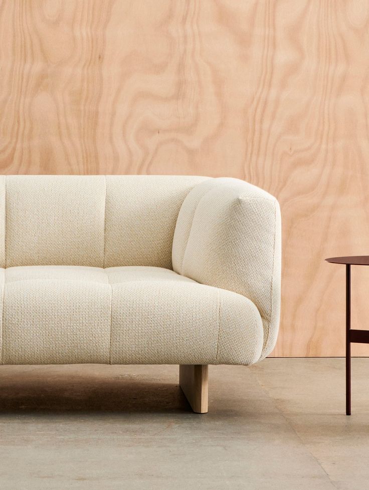 a white couch sitting in front of a wooden wall next to a table and chair