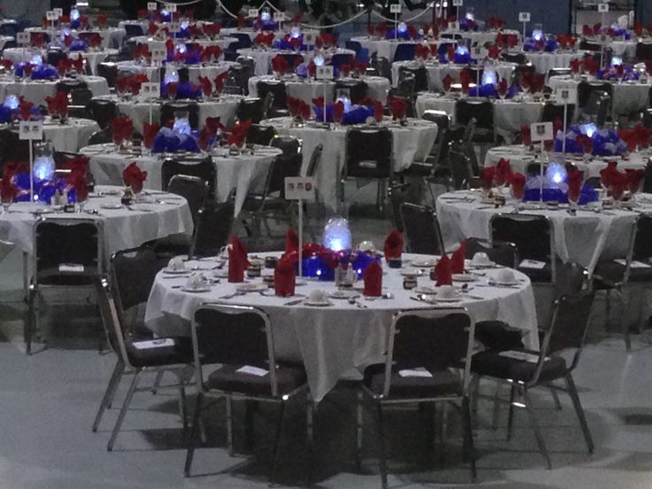 a room filled with lots of tables covered in white and red tablecloths, candles and decorations