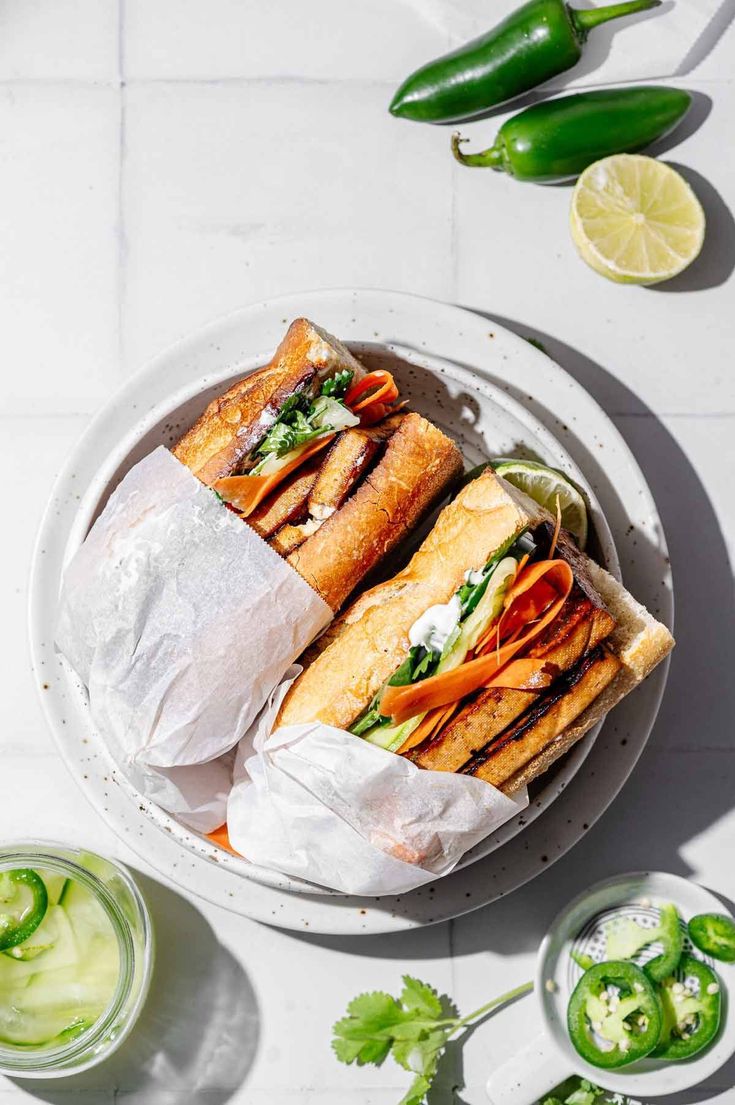 two sandwiches cut in half sitting on top of a white plate next to green peppers