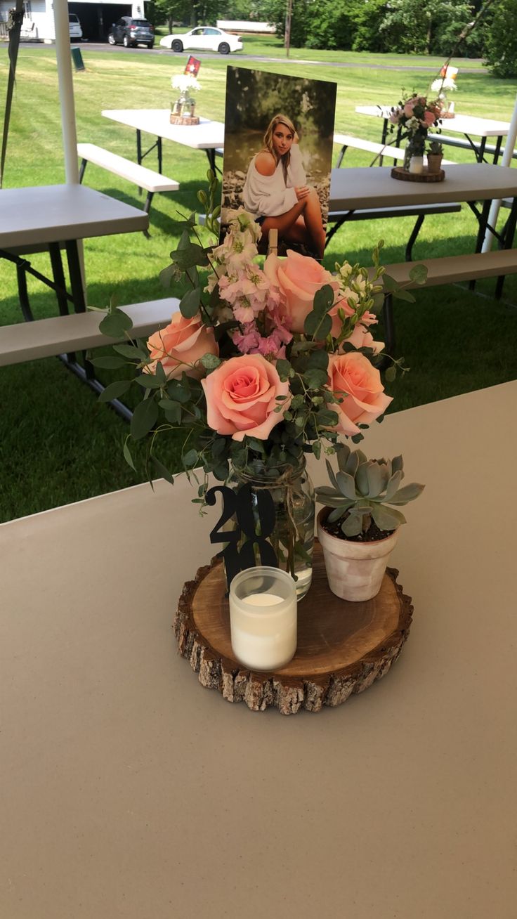 an arrangement of flowers in a vase on a table at a picnic area with tables and benches