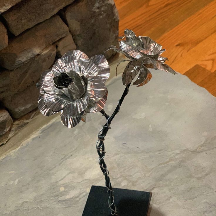 a metal flower on a black stand in front of a stone wall and wood floor