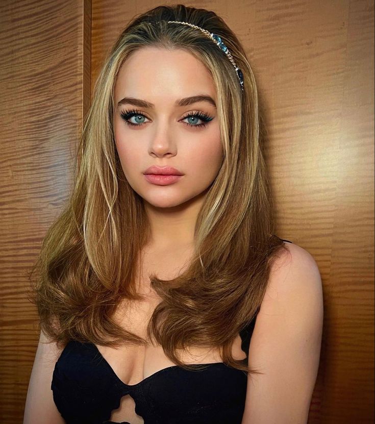 a woman with long hair and blue eyes posing for a photo in front of a wooden wall