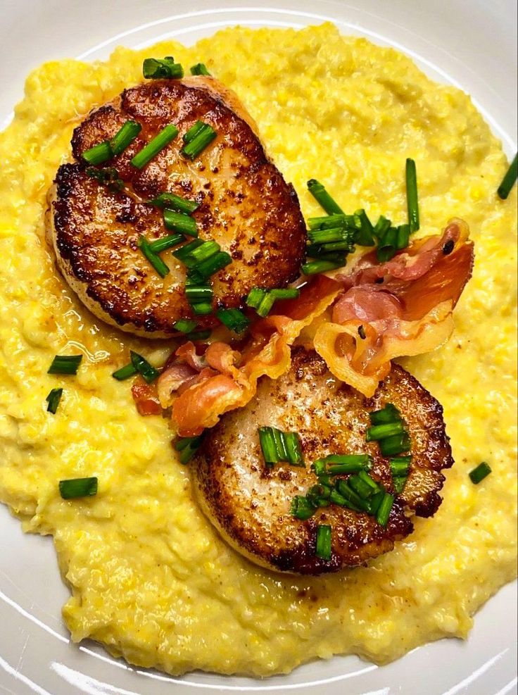 two pieces of meat on top of grits with chives and green onion garnish