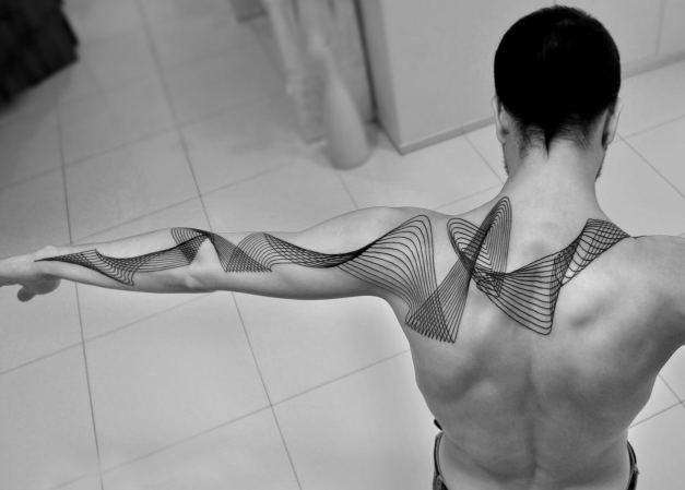 a man with tattoos on his back and arms is standing in front of a tiled floor