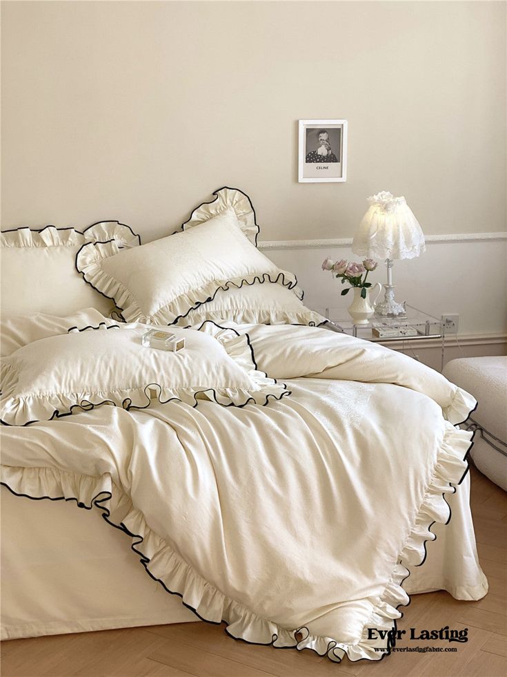 a bed with white sheets and ruffles in a room next to a lamp