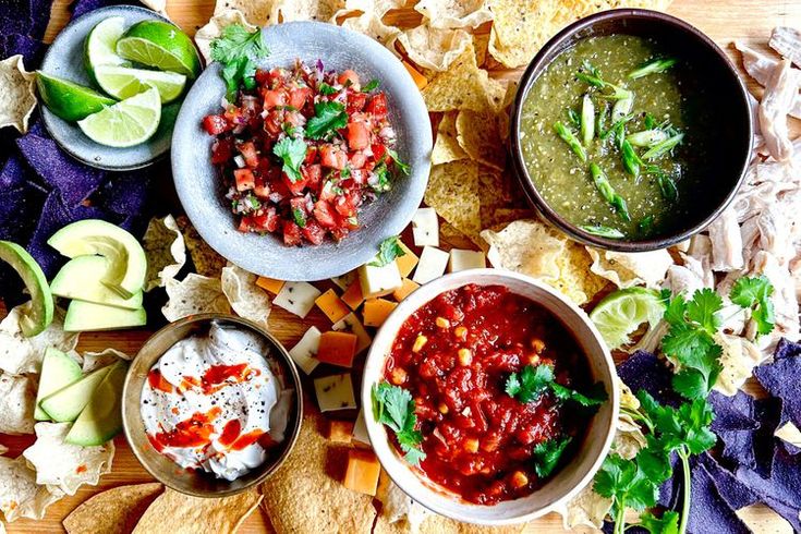 three bowls filled with salsa, tortilla chips and guacamole on a cutting board