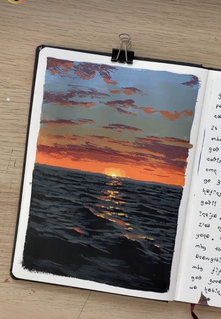 an open notebook with a sunset on the water and some writing in front of it