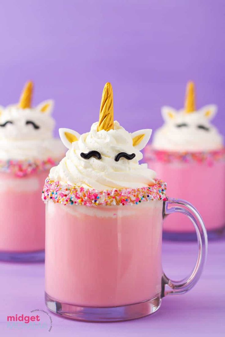 two mugs filled with pink liquid and topped with unicorn face whipped cream, sprinkles