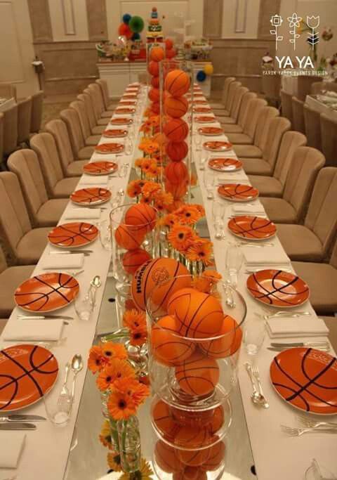 a long table with basketballs and flowers in vases on the top, along with place settings for people to sit at