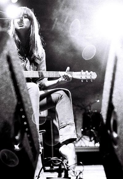 a woman sitting on top of a stool while playing a guitar in front of a microphone