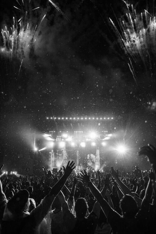 a crowd at a concert with their hands in the air as fireworks go off behind them