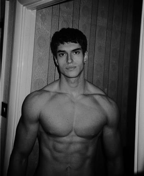 a shirtless young man standing in front of a door and looking at the camera